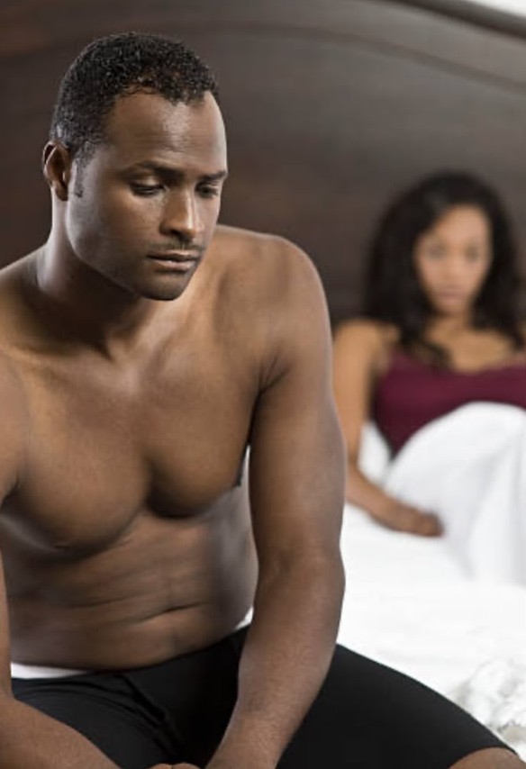 A man sitting on the edge of the bed while a woman rests behind him